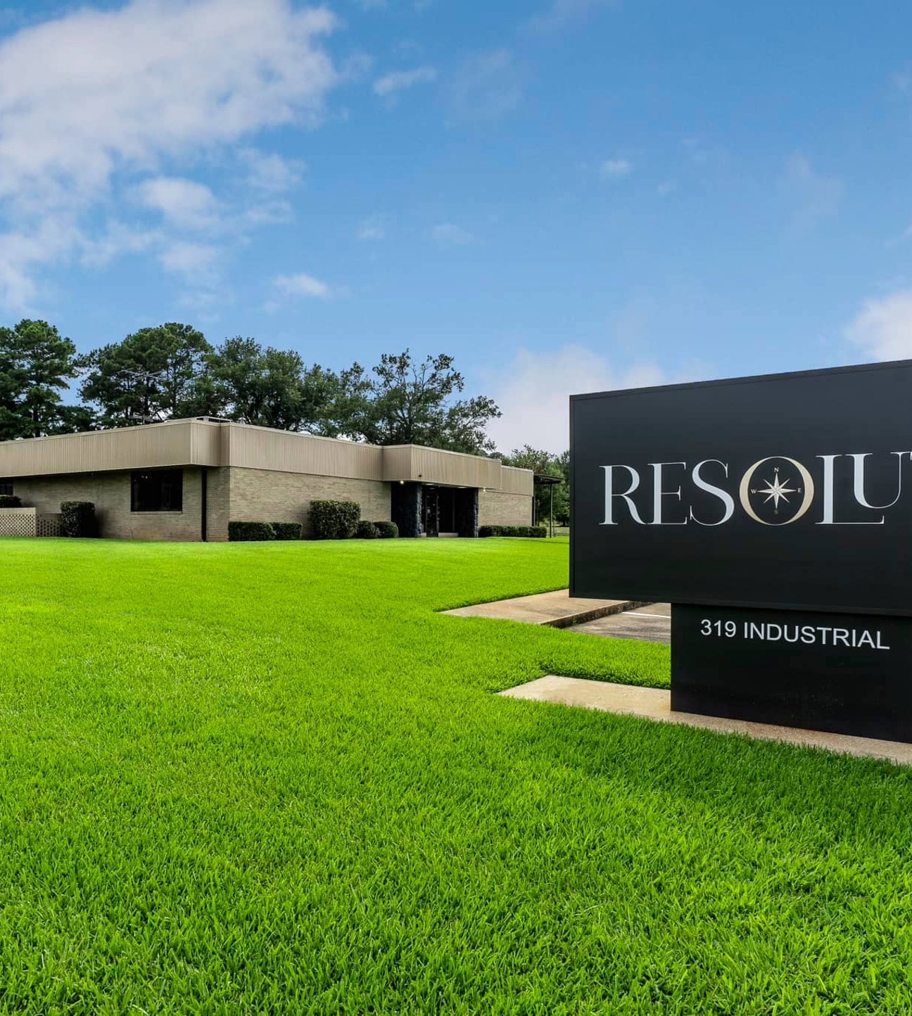 Sign in a field of green grass and in front of an office building and lake, largely displaying Resolute company logo and address.