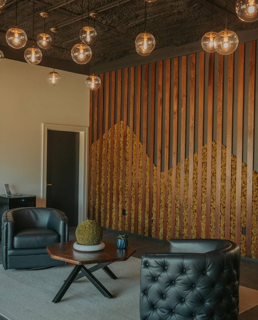 A professional atrium with two leather chairs, a geometric table and plant, and edison bulbs hanging from the ceiling.